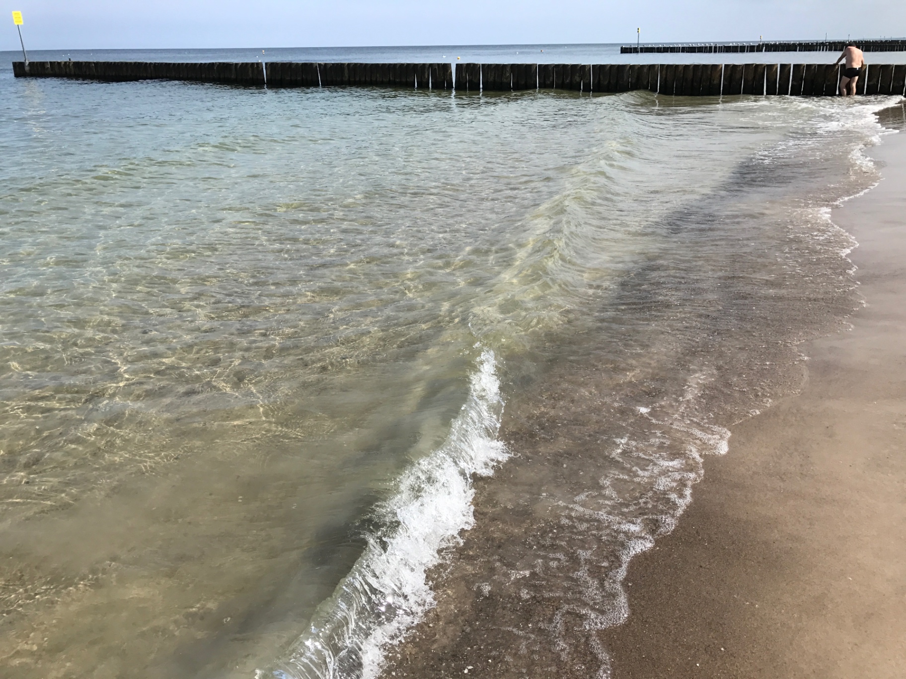 Crystal clear Baltic waves meeting the sandy shore - wooden breakwaters in the background on a summer day