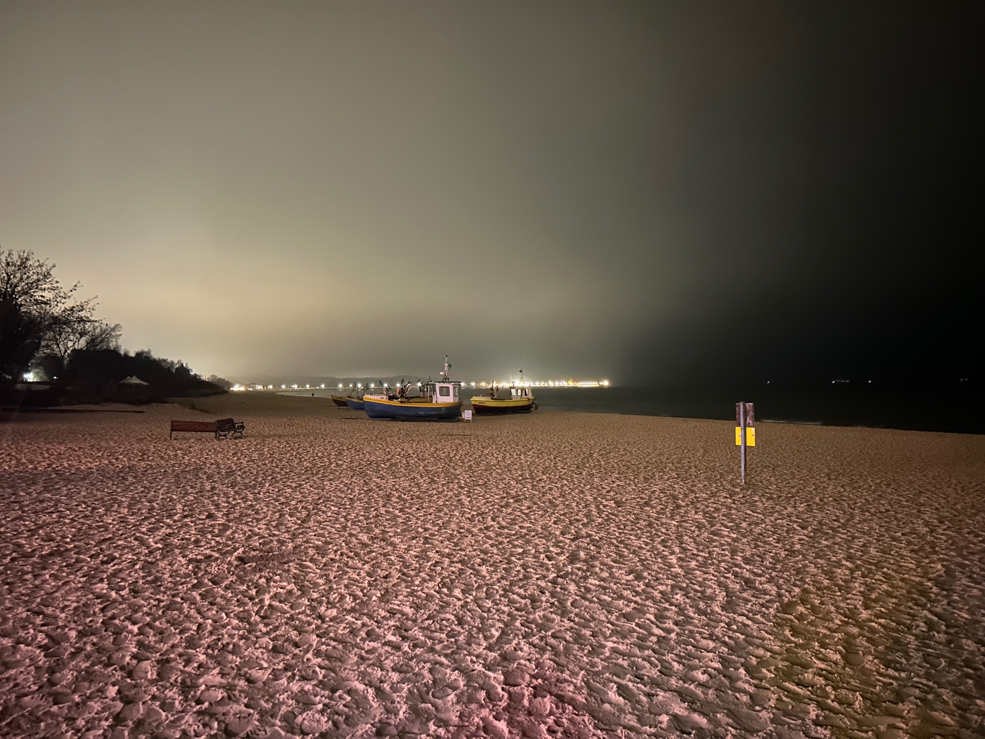 Fishing boats on the beach at night - the atmospheric glow of distant city lights reflecting on the calm sea