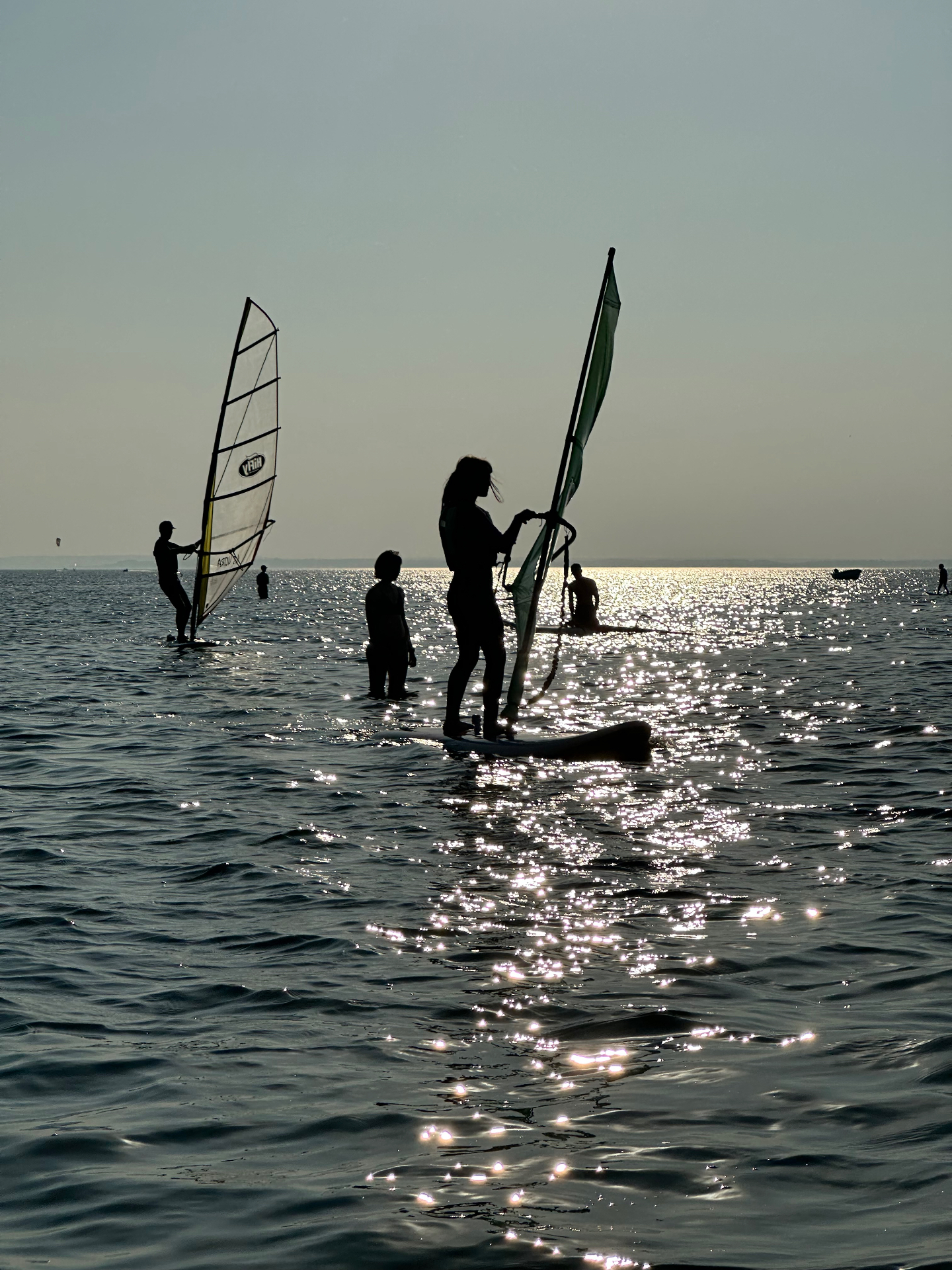 Silhouettes of windsurfers at golden hour - the sparkling water reflecting the setting sun
