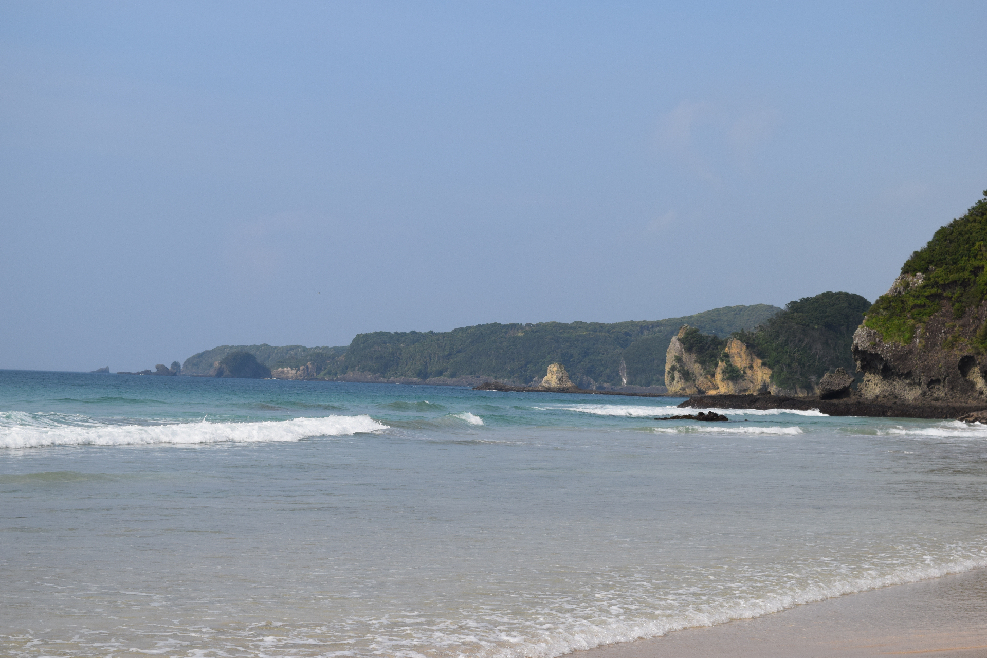 A tranquil Japanese bay with crystal-clear waters - rocky cliffs and forested hills along the scenic coastline