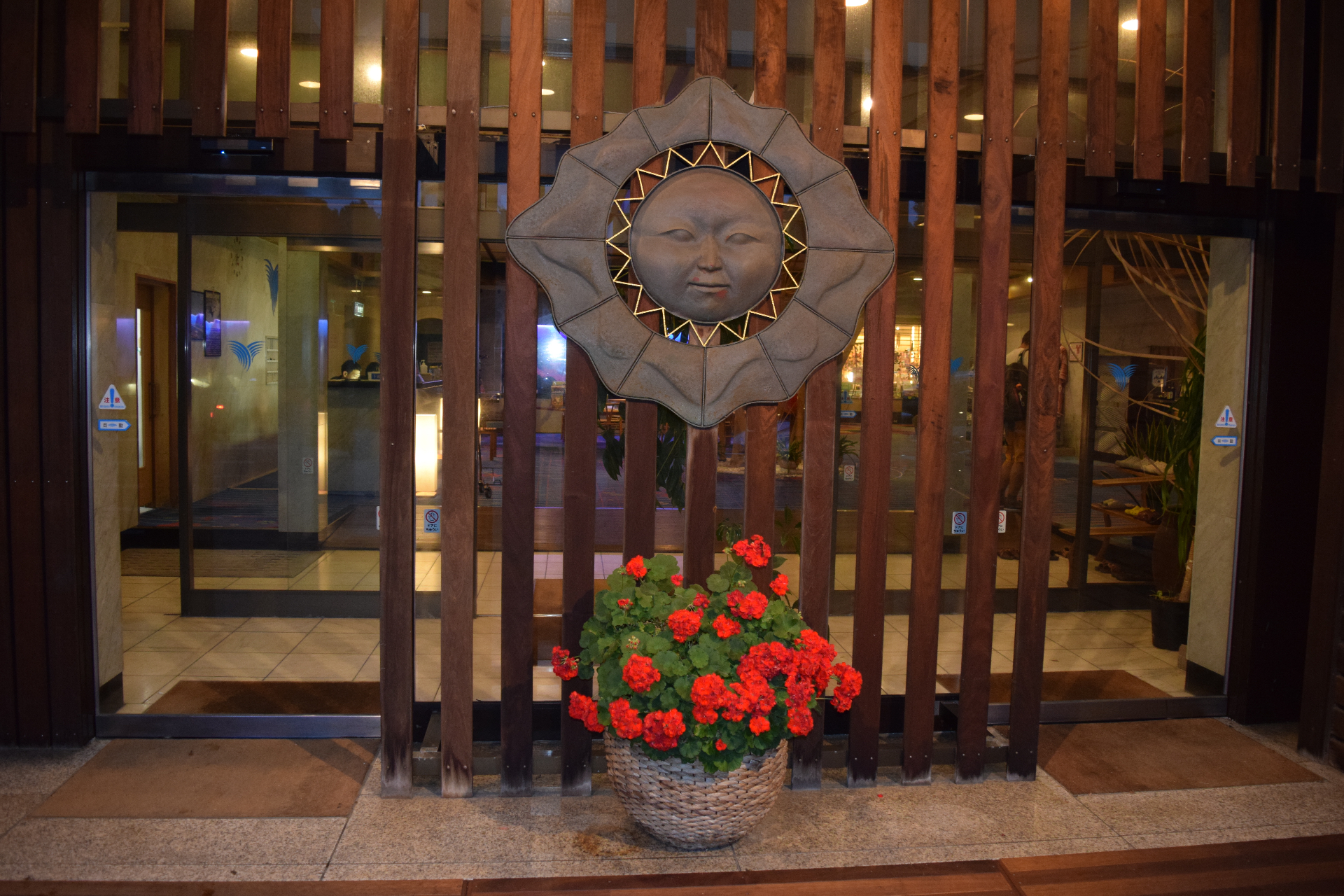 Traditional sun face sculpture at a hotel entrance - artistic Japanese hospitality with red geraniums