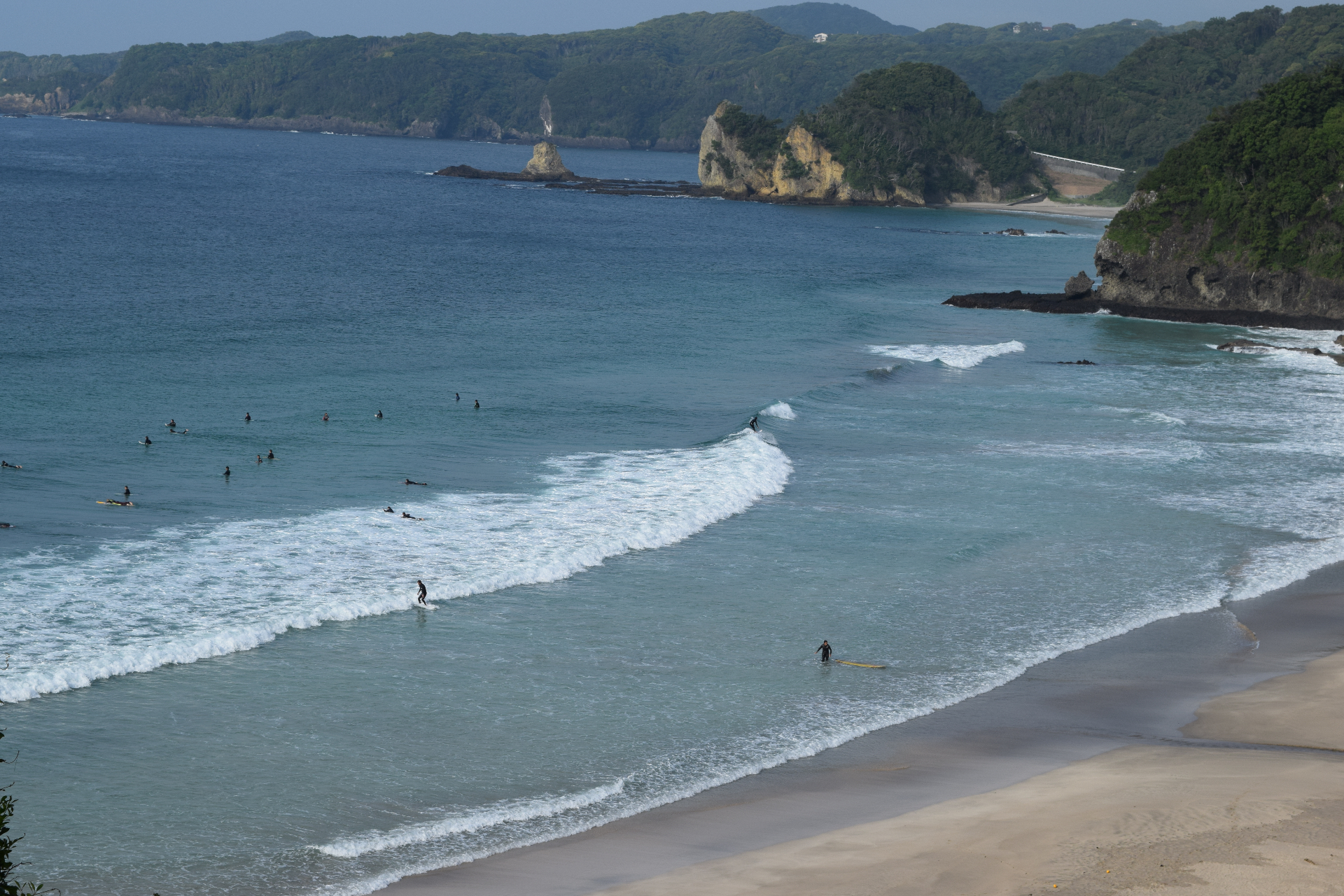 Surfers catching waves on a Japanese beach - the beautiful coastline with dramatic cliffs in the background