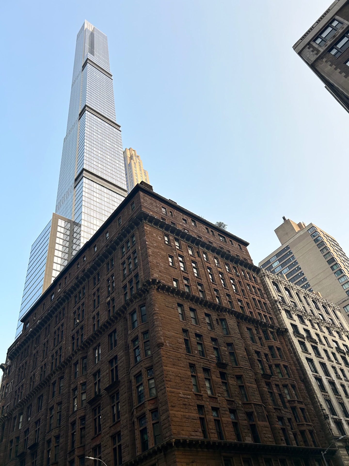 Steinway Tower rising above classic brownstone buildings - the slender supertall skyscraper contrasting with historic Midtown architecture